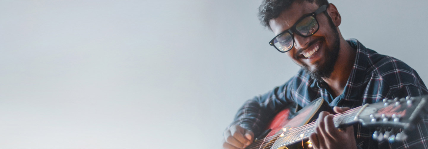 Man with glasses and plaid shirt smiling and playing guitar - diversity equity inclusion.