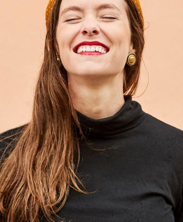 a smiling woman wearing a black turtleneck with long hair and closed eyes.