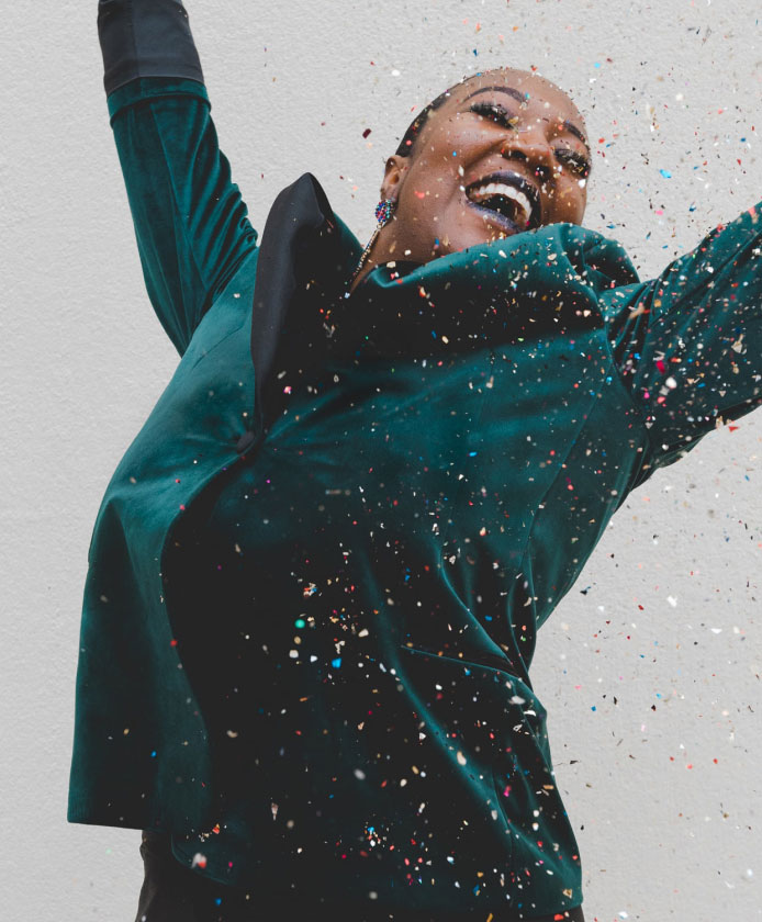 Woman in a green velvet suit jumping with hands up with confetti falling around her - internal communications jobs.